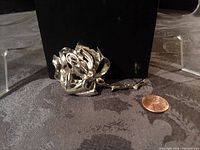 Front view of silvertone rose brooch photographed beside a US penny for scale, showing detailed petals and shiny metal finish.