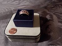 Silvertone ring displayed on a blue velvet ring box with a penny nearby for scale, showing overall design and size.