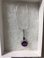 Overall view of pendant with chain inside white box with padding.