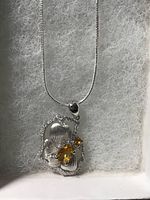 Front view of the pendant showing the flower design with citrine and white CZ on silver chain against a white padded surface.