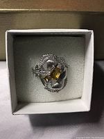 Front angled view of citrine and cubic zirconia flower ring in white gold over 925 silver, inside white box.