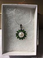 Pendant with green marquise-shaped chrome diopside stones in a circular flower pattern around a large central white pearl on a silver-colored chain, displayed in a white box with padding.