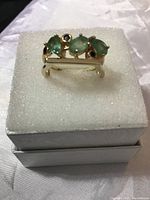 Emerald and black spinel ring shown sitting on white foam inside a box, angled to show side profile and setting details.