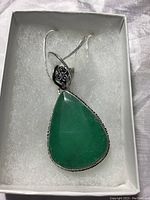 Full view of tear drop green pendant with silver chain in a white cushioned box