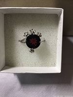 Top-down view of garnet stone and CZ flower accents on the ring inside white box.
