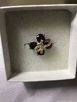 Ring with pear cut red garnet stones and white CZ on a 14k white gold over 925 band inside a gray padded box.