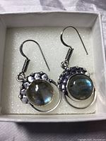 Photo of both earrings in a white box with foam padding showing front view of silver earrings with round labradorite stones