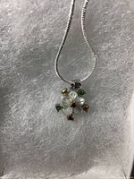 Top-down photo of mother of pearl flower pendant with multi-colored gemstone accents on a white surface showing pendant and chain