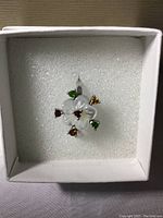 Top view of mother of pearl flower ring with colored gemstones in white box.