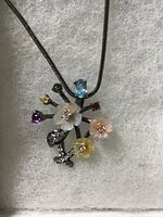 Photo of the mother of pearl flower pendant with assorted gemstones on black rhodium chain displayed on a textured white background.