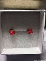 Front view of the two round fire opal stud earrings with orange to reddish-pink color set in prong rose gold settings inside a white jewelry box cushioned with foam.