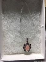 Pendant with oval pink opal center surrounded by raspberry red rhodolite garnets, on 14k white gold over 925 silver chain, in white box with padding