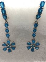 Front view of two hanging flower earrings with pear cut Paraiba apatite stones in white gold setting.