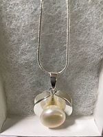 Close-up front view of pearl pendant with white gold over 925 silver setting, showing the round button creamy white pearl and bail, against soft gray lining.