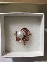Ring featuring a white pearl, pink tourmaline stones, and black spinel accents in a white box on a gray background.
