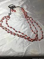 Photo of a hand knotted pink Baroque pearl necklace laid out on a light, crumpled fabric background, showing its length and the irregular shapes of the pearls. The necklace is in new condition and approximately 30-34 inches long.