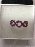 Top view of ruby ring showing 'XOX' design with multiple prong-set ruby stones in 14k white gold over 925 silver band, displayed in white cushioned box.