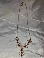 Full length photo of the necklace laid out in a straight line showing chain and floral pendant.