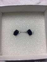 Front view of pair of blue sapphire stud earrings on white foam in box