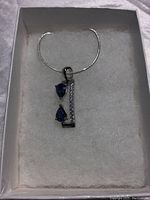 Pendant featuring two pear cut blue sapphires and a vertical row of white cubic zirconia set in white gold over silver, shown in a box with chain.