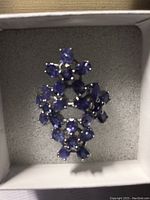 Close-up image of the tanzanite flower ring showing the multiple oval and round purple-blue stones in floral arrangement inside a white cushioned box.