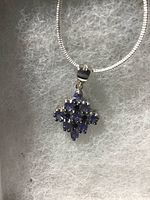 Photo of blue-violet oval cut tanzanite and black spinel pendant set in 14k white gold over 925 silver against a textured background.
