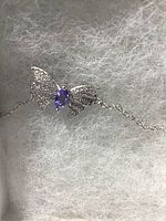 Close-up photo of the butterfly centerpiece of the bracelet showing the violet blue marquis cut tanzanite gemstone centered between wings studded with white cubic zirconia. The butterfly design is in shiny 14k white gold over 925 sterling silver with a delicate chain attached.
