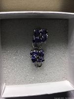 Top view of pair of earrings showing deep blue tanzanite clusters and cubic zirconia in white gold setting inside cushioned box.