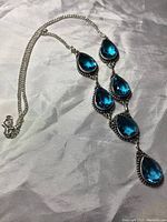 Full view of silver necklace with seven pear cut blue topaz stones arranged vertically, displaying the entire piece with chain and clasp.