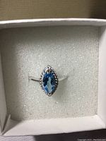 Top view of marquis cut blue Swiss Topaz ring with white cubic zirconia accents in a white cushioned box.
