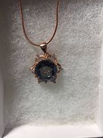 Close-up front view of the pendant showing the round cut mystic topaz surrounded by white CZ stones in a rose gold setting on a matching chain inside a box.