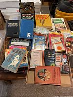 Photo showing a collection of books spread out on a surface including dictionaries, cookbooks, and various other subjects with some CDs nearby.