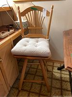 Front view of the wooden bar height swivel chair with attached cream tufted cushion, showing leg base and swivel design.