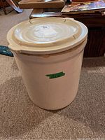 Front view showing full crock with lid and visible chips on lid edges, and a green sticker on side.