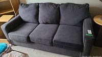 Front view of dark gray three-seater fabric sofa bed with three cushions including seat and back cushions, showing overall condition and form.