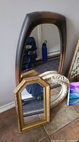 Three framed wall mirrors: large brown rectangular, medium gold rectangular, and oval white distressed.