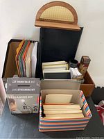 Photo showing live streaming kit box alongside colorful file folders, books, and stationery boxes arranged in a wooden desk organizer and storage boxes