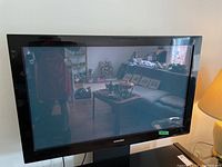 Front view of Samsung TV showing black bezel, reflective screen, and room reflection.