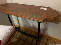 Side view of wood side table showing decorative inlay and shaped edges on top, turned black legs, and horizontal support bar.