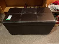 Front view of brown faux leather storage bench with padded, stitched top and minor wear.
