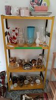 Full view of yellow metal storage shelf filled with various glassware, ceramics, and kitchen items.