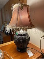 Front angled view of the table lamp showcasing the leather base, decorative metal conchos, leather straps, and fabric shade with feathered fringe.