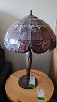 Full front view of the Tiffany style lamp showing the stained glass shade and base on a wood table.