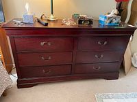 Front view of vintage six drawer wood dresser with items on top.