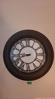 Front view of vintage-style wall clock with Roman numerals and openwork face mounted on wall