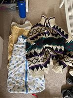 Image of the wool sweater and two baby bunting outfits laid on carpet.