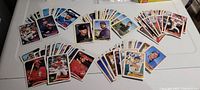 Photo of a large assortment of 1988 Topps baseball cards featuring players from various National League Central teams such as Cubs, Pirates, Cardinals, Brewers, and Reds. Cards are fanned and stacked on a white surface, showing front images of many cards.