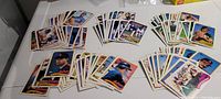 Eight distinct piles of 1988 Topps baseball cards laid out, showing various players from Astros, Rangers, Mariners, Angels, and Athletics teams grouped separately.