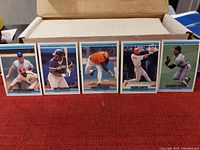 Photo showing a row of 5 1992 Donruss baseball cards (players include Mark Grace, Barry Bonds, Frank Viola, Oscar Gamble, Randy Ready) standing in front of a box holding hundreds of similar cards.