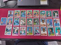 Photo showing 26 different Topps baseball cards laid out on a dark surface beneath a laptop keyboard.